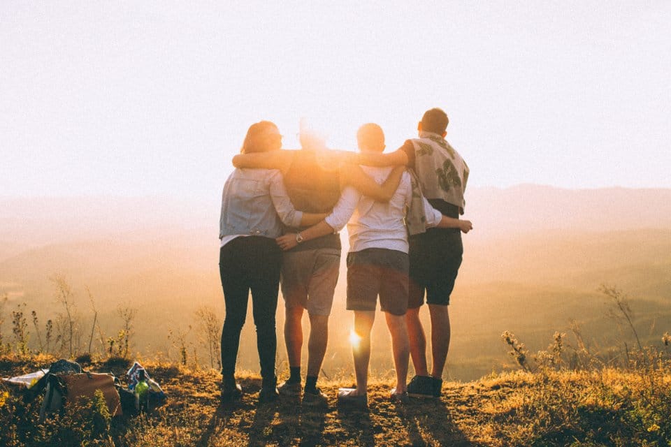 Friends standing together arm in arm at sunset