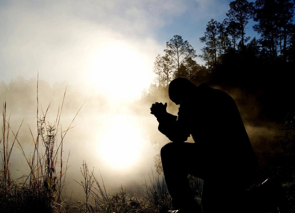 Man kneeling in prayer at sunrise