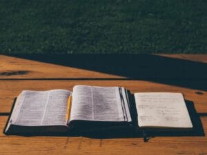 Open Bible and notebook on a table in sunlight