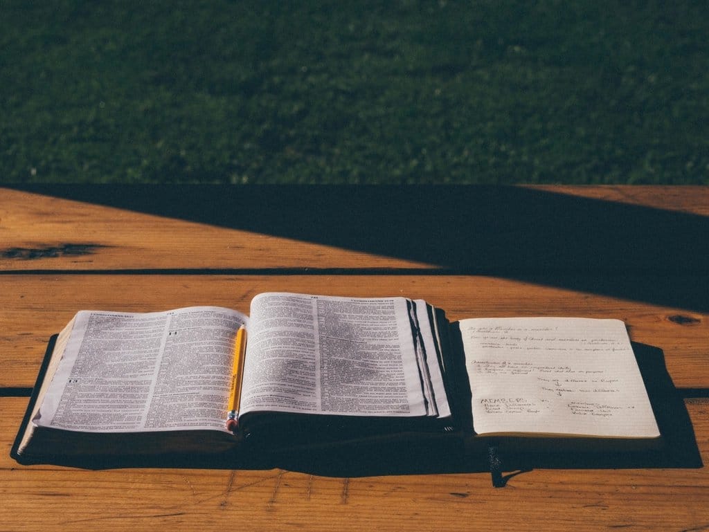 Open Bible and notebook on a table in sunlight